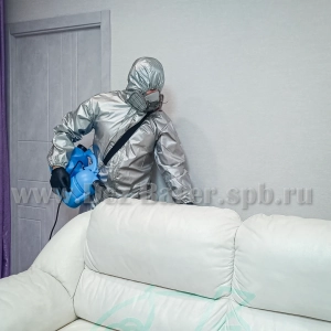 дезинфектор в защите обрабатывает белый диван наклонившись над спинкой