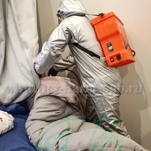 Дезинфектор в защите обрабатывает одеяло и подушки на кровати в спальне
