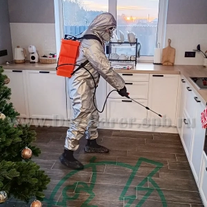Дезинфектор в защите обрабатывает пол и кухонные поверхности в комнате с ёлкой